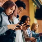 High school student and her friends using their smart phones in a hallway.